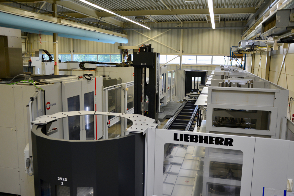 Un robot (au centre) se déplace sur des rails entre les deux fraiseuses (à gauche) et le magasin à palettes (à droite). La cellule complète mesure environ 20 mètres de long sur 10 de large